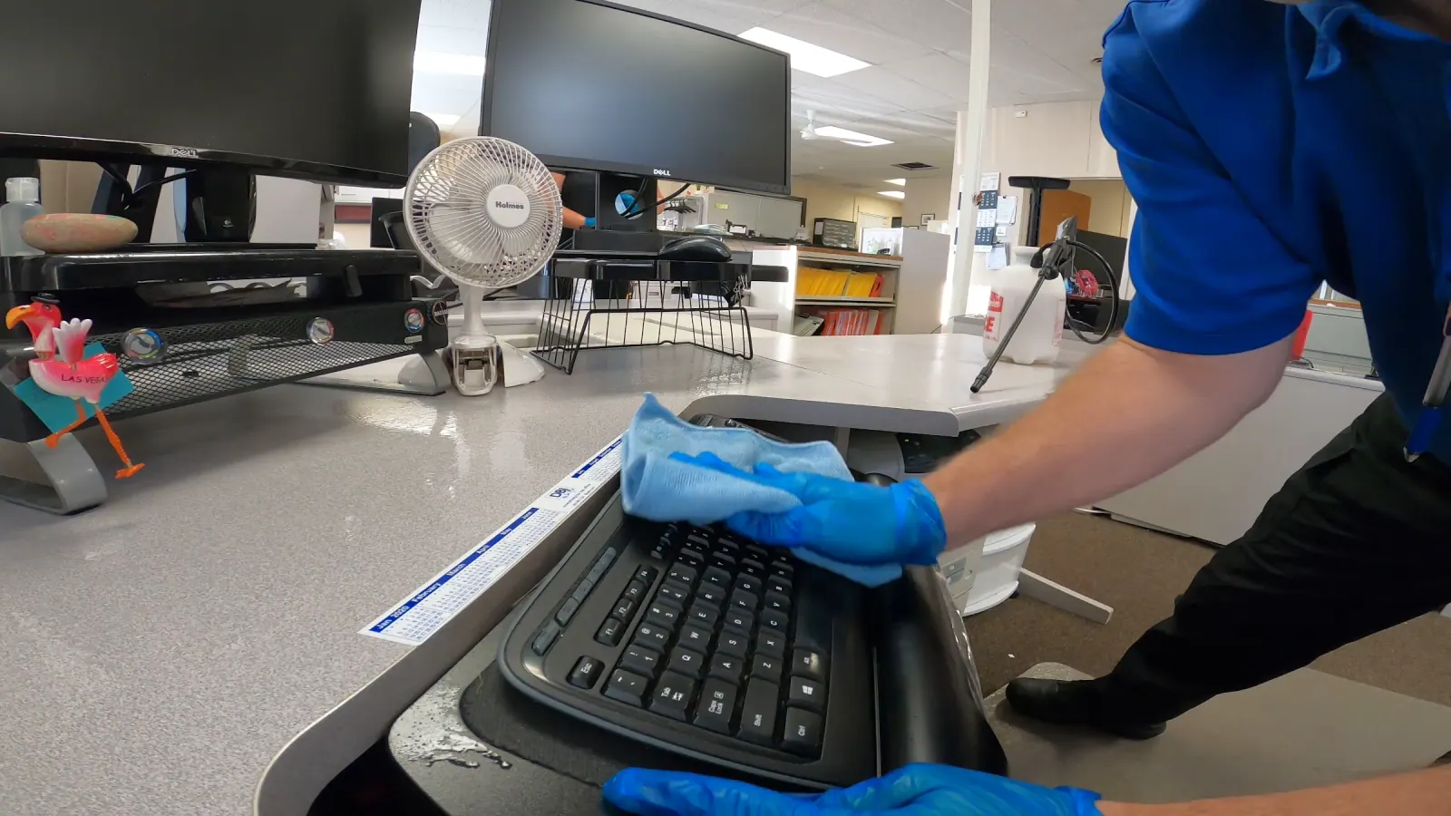 Gloved technician wiping a keyboard at an office workstation